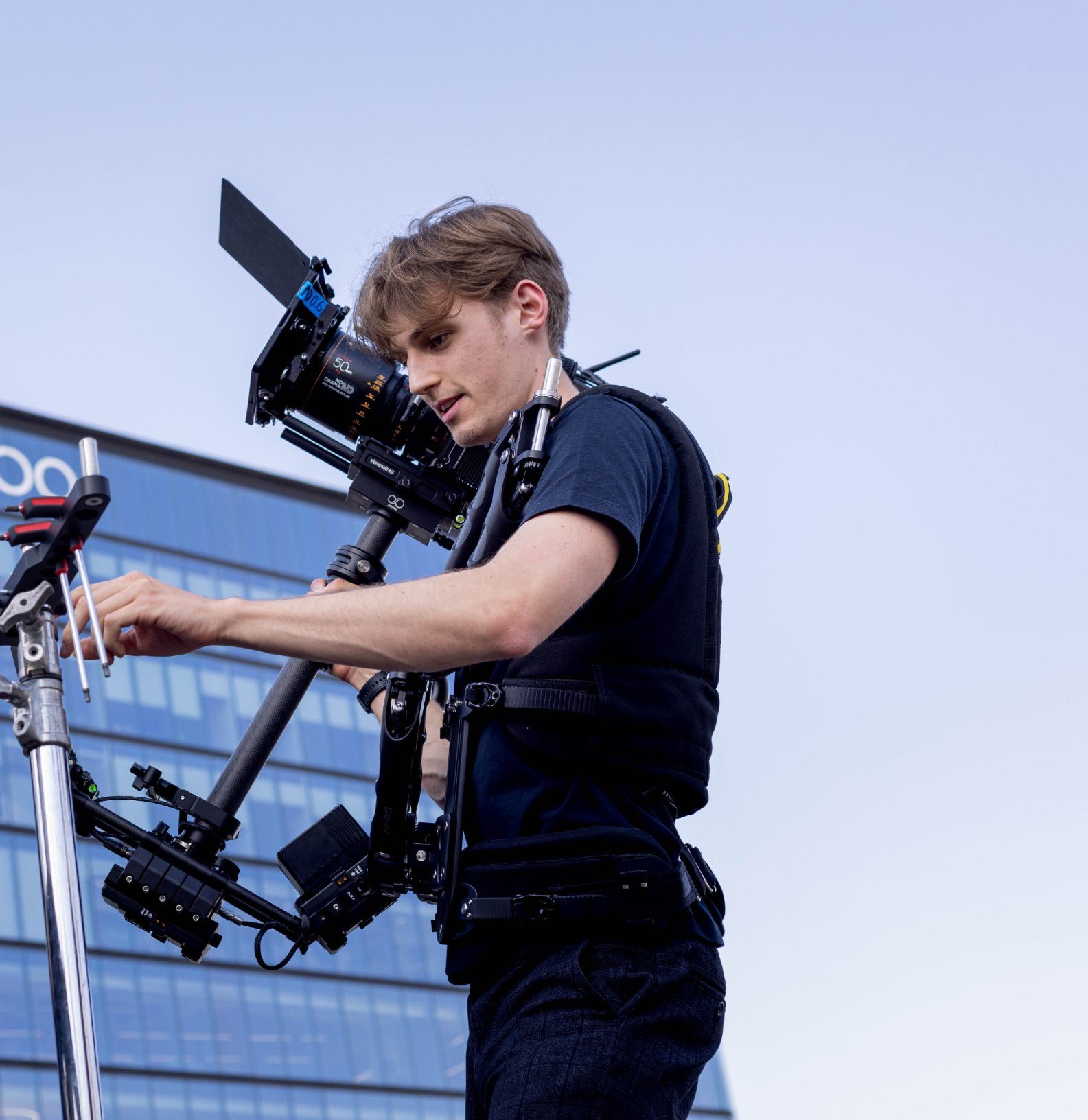 Daniel Hodász balancing a Steadicam rig on set, with a glass office building behind him